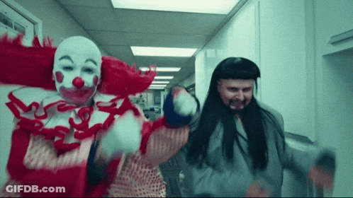 A Man Dressed As A Clown And Another Man Dressed As A Prisoner Are Dancing In A Hallway GIF