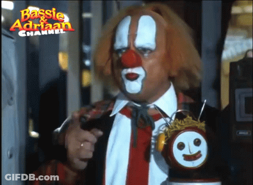A Man Dressed As A Clown Is Holding A Clock With A Face On It And The Words Basisie & Adrian Channel Above Him GIF