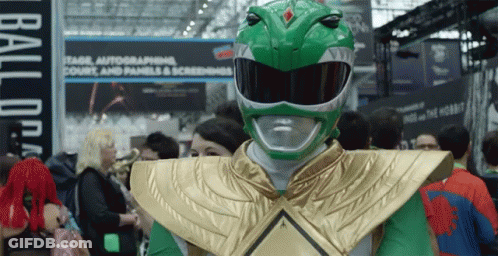 A Man Dressed As A Green Power Ranger Stands In A Crowd Of People GIF