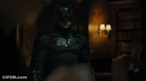 A Man Dressed As Batman Stands In A Dark Room GIF