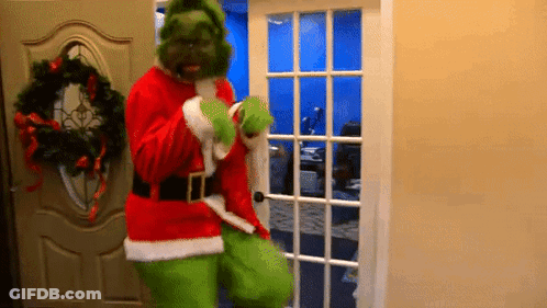 A Man Dressed As Grinch Is Standing In A Doorway . GIF