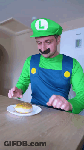 A Man Dressed As Luigi From Super Mario Is Eating A Donut GIF