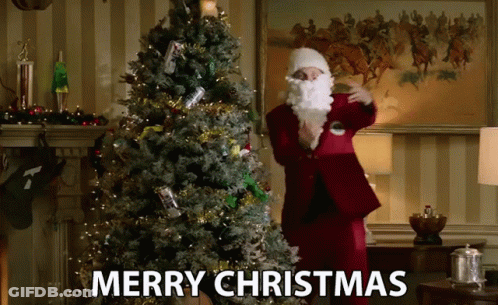 A Man Dressed As Santa Claus Is Standing In Front Of A Christmas Tree With The Words Merry Christmas Below Him GIF