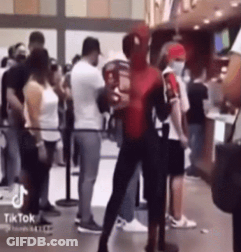 A Man Dressed As Spider Man Is Standing In Front Of A Crowd Of People . GIF