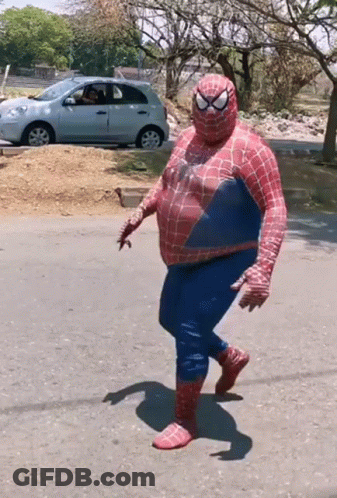 A Man Dressed As Spider Man Is Walking Down The Street GIF