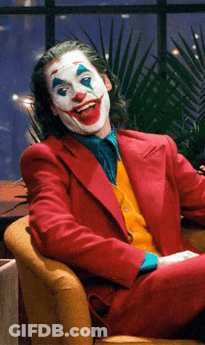 A Man Dressed As The Joker Sits In A Chair GIF