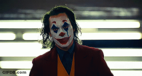 A Man Dressed As The Joker With A Clown Face Painted On His Face . GIF