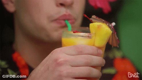 A Man Drinking A Pineapple Juice With A Green Straw From A Glass That Says Brat On The Bottom GIF