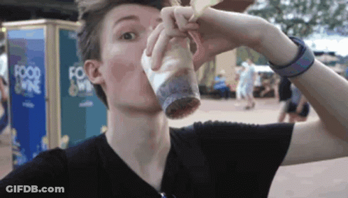 A Man Drinking From A Cup In Front Of A Food Kiosk GIF