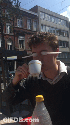 A Man Drinking From A Cup With A Plastic Spoon In His Eye GIF