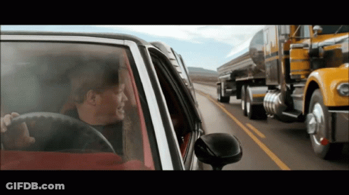 A Man Driving A Car On A Highway Next To A Semi Truck That Says Peterbilt On It GIF