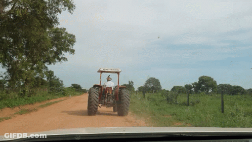 A Man Driving A Tractor On A Dirt Road With A Roof That Says ' New Holland ' On It GIF