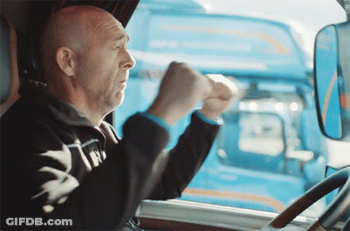 A Man Driving A Truck With A Blue Truck In The Back GIF