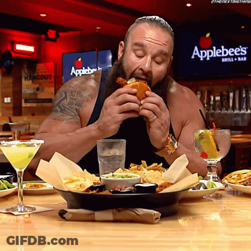 A Man Eating A Hamburger In Front Of A Sign That Says Applebee 'S GIF