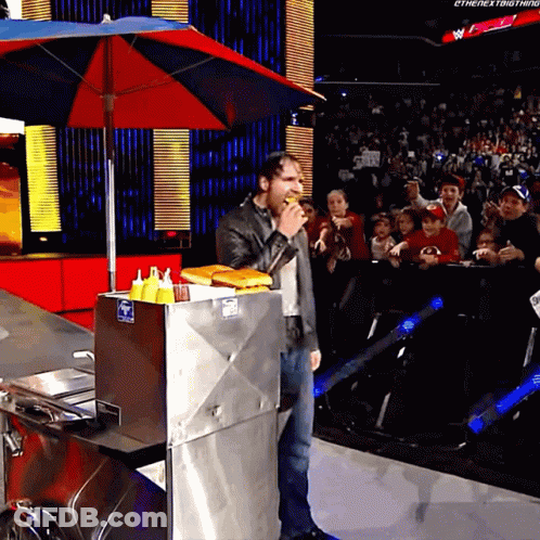 A Man Eating A Hot Dog In Front Of A Crowd That Says The Next Thing GIF