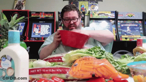 A Man Eating A Salad In Front Of A Mortal Kombat Video Game GIF