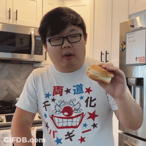 A Man Eating A Sandwich In Front Of A Refrigerator With Groceries On It GIF