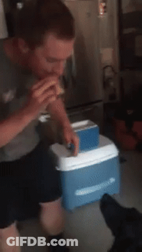 A Man Eating A Sandwich Next To An Ice Box GIF