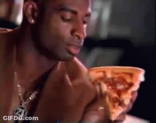 A Man Eating A Slice Of Pizza With The Number 21 On His Necklace GIF