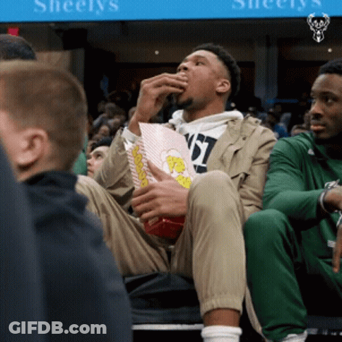 A Man Eating Popcorn In Front Of A Sign That Says Sheelys GIF