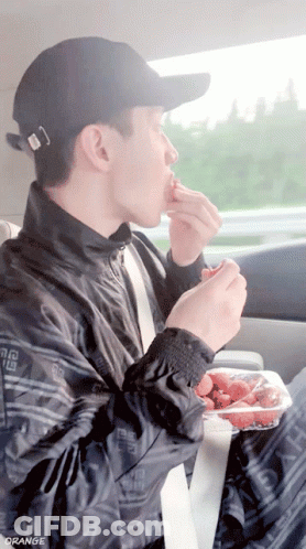 A Man Eating Strawberries In A Car With The Word Orange On The Bottom Right GIF