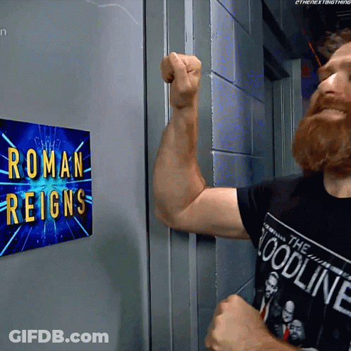 A Man Flexes His Arm In Front Of A Roman Reigns Sign GIF