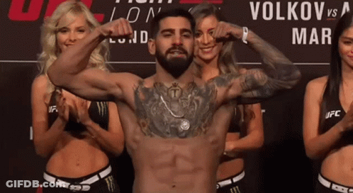 A Man Flexes His Muscles In Front Of A Sign That Says Volkov On It GIF