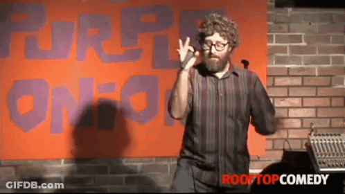A Man Giving A Speech In Front Of A Sign That Says Rooftop Comedy GIF