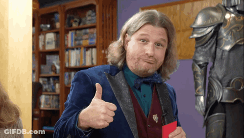 A Man Giving A Thumbs Up In Front Of A Bookshelf GIF