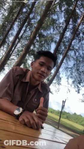 A Man Giving A Thumbs Up In Front Of Trees GIF