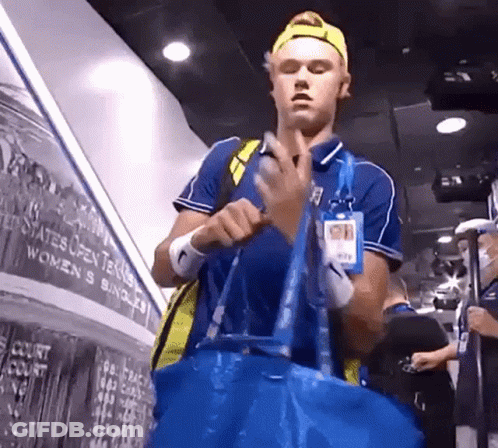 A Man Holding A Blue Bag In Front Of A Wall That Says ' United States Open Tennis ' On It GIF