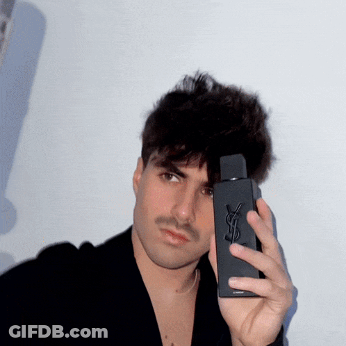 A Man Holding A Bottle Of Yves Saint Laurent Cologne GIF
