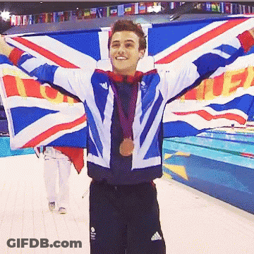 A Man Holding A British Flag With His Arms Outstretched And A Medal Around His Neck GIF