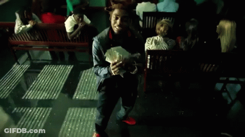 A Man Holding A Bunch Of Money In Front Of A Group Of People Sitting On Benches GIF