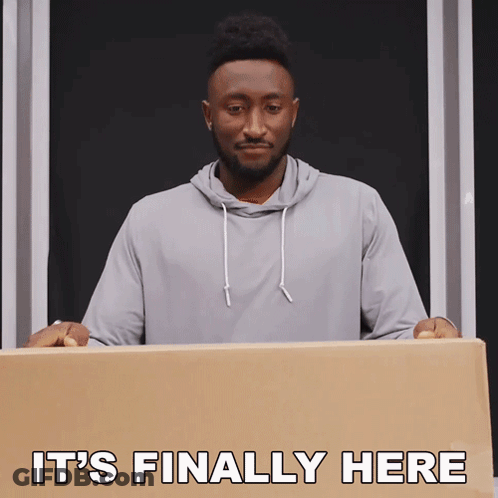 A Man Holding A Cardboard Box With The Words " It 'S Finally Here " Above Him GIF