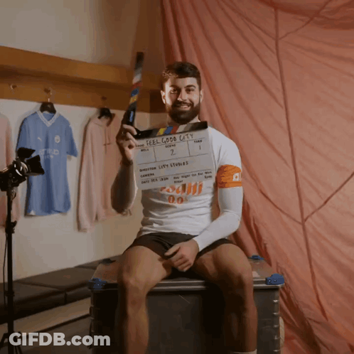 A Man Holding A Clapper Board That Says Feel Good Cats On It GIF