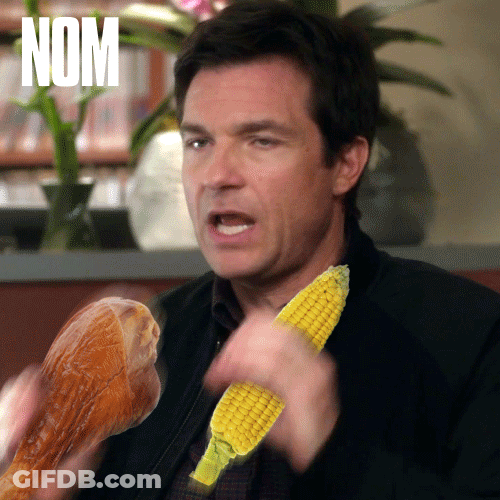 A Man Holding A Corn On The Cob And A Chicken Leg With The Word Nom On The Bottom Right GIF
