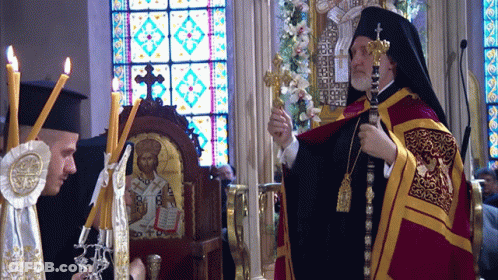 A Man Holding A Cross Stands In Front Of A Stained Glass Window GIF