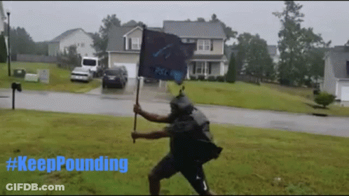 A Man Holding A Flag In The Rain With #Keeppounding Written In Blue GIF