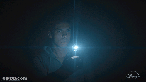 A Man Holding A Flashlight In A Dark Room With A Disney + Logo GIF