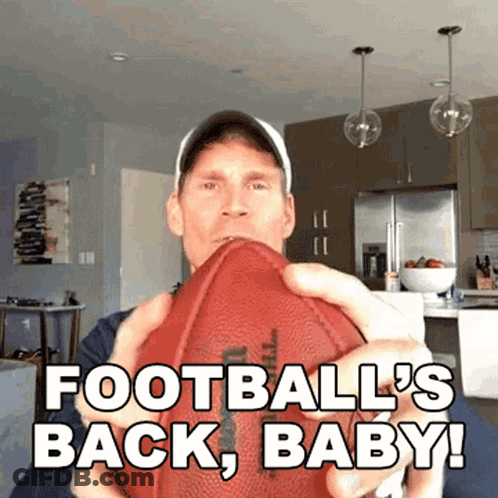 A Man Holding A Football With The Words " Football 'S Back Baby " GIF