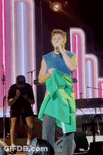 A Man Holding A Green And Yellow Flag On Stage GIF