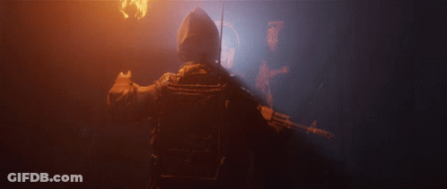 A Man Holding A Gun In A Dark Room With A Light Behind Him GIF
