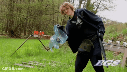 A Man Holding A Gun In A Field With The Word Bgs On The Bottom Right GIF