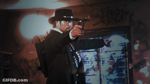 A Man Holding A Gun In Front Of A Window With Graffiti On It GIF