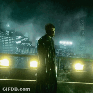 A Man Holding A Gun Stands In Front Of A City At Night GIF