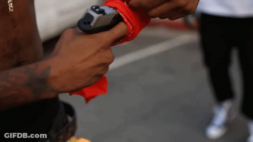 A Man Holding A Gun With A Red Bandana Around His Thumb GIF