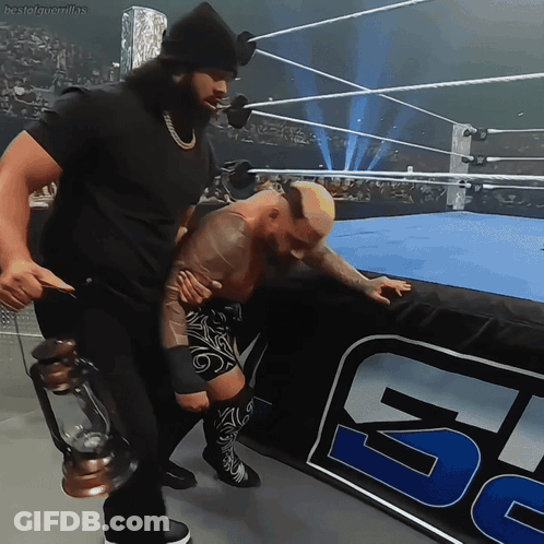 A Man Holding A Lantern Stands Next To A Wrestler In A Ring GIF