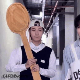 A Man Holding A Large Wooden Spoon In A Hallway . GIF