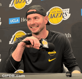 A Man Holding A Microphone In Front Of A Lakers Logo GIF